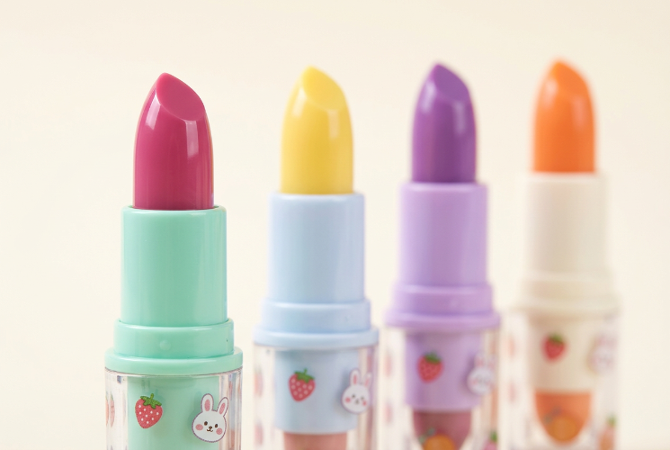 Close up of four pastel Lip Color Changing Lipstick tubes in pink yellow purple and orange with strawberry and bunny stickers on a cream background.